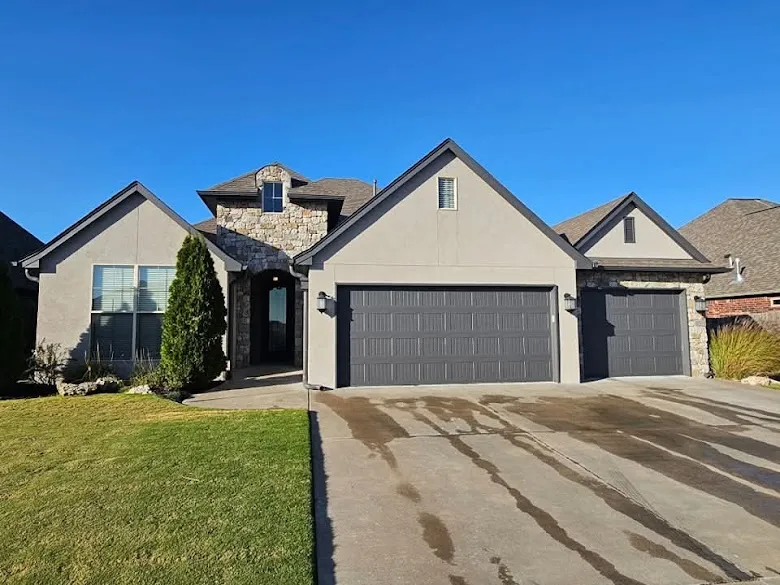 Stucco and stone home with gray garage doors and a freshly washed driveway
